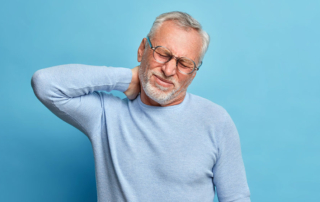 Older man suffering from pain in neck, rubs his neck and grimaces from pain